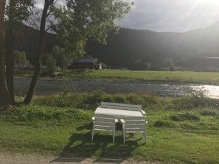 Bord og stoler på gress ved en elv med utsikt